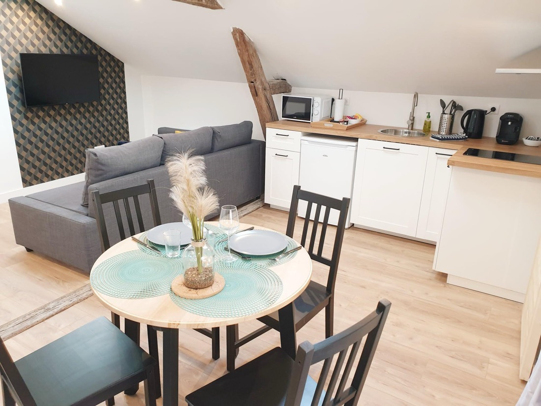 Pièce de vie sous les combles avec cuisine équipée, table dressée et canapé